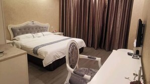 Quarto de hotel com uma cama, escrivaninha, cadeira e uma janela grande com cortinas.