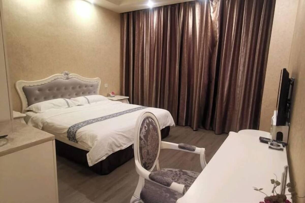 A hotel room with a bed, a desk, a chair, and a large window with curtains.