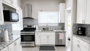 Une cuisine moderne avec des meubles blancs, une cuisinière, un four et un four à micro-ondes.