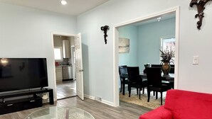 A living room with a TV, glass coffee table, red sofa, and a dining area with chairs and a table. - Lincoln Ave Home By Naval Base! (North Chicago)