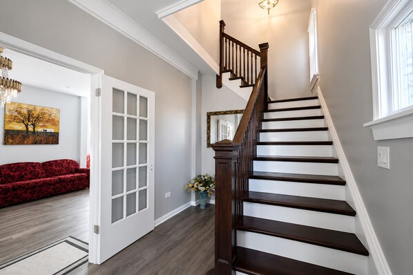 A staircase with dark wood steps and white trim, a red sofa in a room with a wooden floor, and a painting on the wall.