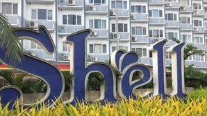 A sign with the word "Shell" in large blue letters, surrounded by yellow plants. - Nice and Simple 1 Bedroom in Shell Residences (Pasay)
