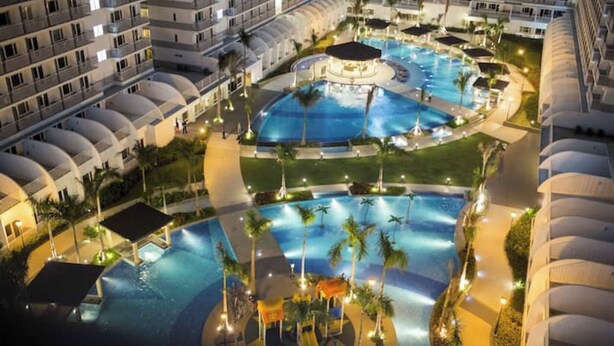 A hotel with multiple swimming pools, palm trees, and a well-lit outdoor area. - Nice and Simple 1 Bedroom in Shell Residences (Pasay)