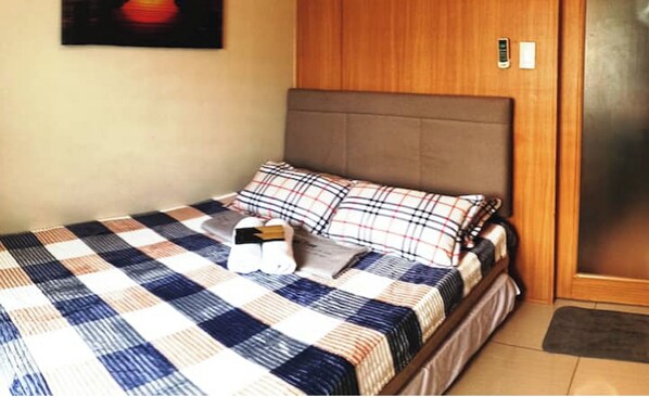 A neatly made bed with a plaid bedspread, a pillow, and a folded towel.