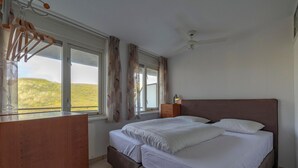 A bedroom with a bed, a wooden dresser, a nightstand, and a window with curtains. - Apartment in Callantsoog Near Beach Access (Callantsoog)