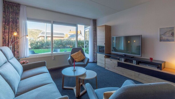 Una sala de estar moderna con un sofá, un sillón y un televisor sobre un soporte de madera.