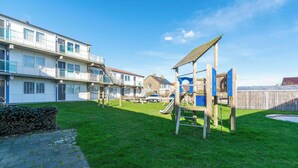 Un barrio residencial con un parque infantil, un camino pavimentado y edificios de varios pisos con balcones.