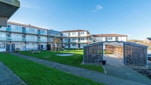 Un patio con un parque infantil, una zona de estar cubierta y un edificio con varios balcones y ventanas.