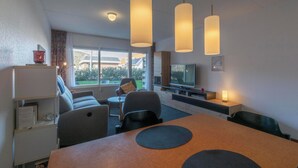 Habitación de hotel moderna con comedor, sofá, televisión y un amplio ventanal con vistas al exterior.