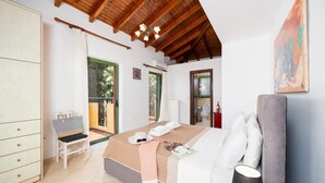 A bedroom with a bed, a chair, a wardrobe, and a balcony. - Villa Poseidonia - Three Bedroom Villa, Sleeps 6 (Ionian Islands)