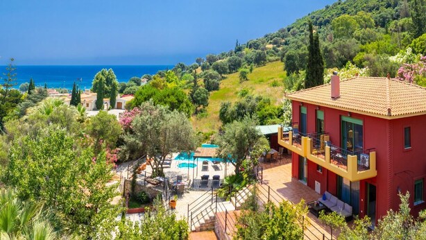 A red villa with a pool, surrounded by lush greenery and a view of the sea. - Villa Poseidonia - Three Bedroom Villa, Sleeps 6 (Ionian Islands)