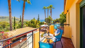 Ein Balkon mit Tisch und Stühlen, der auf eine Küstenlandschaft mit Palmen und blauem Himmel blickt.