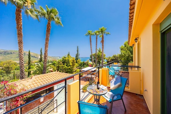 Ein Balkon mit Tisch und Stühlen, der auf eine Küstenlandschaft mit Palmen und blauem Himmel blickt.