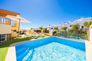 A swimming pool with lounge chairs, a pergola, and modern white buildings in the background.