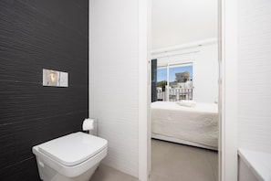 A modern bathroom with a toilet, a towel dispenser, and a window with a view of buildings.