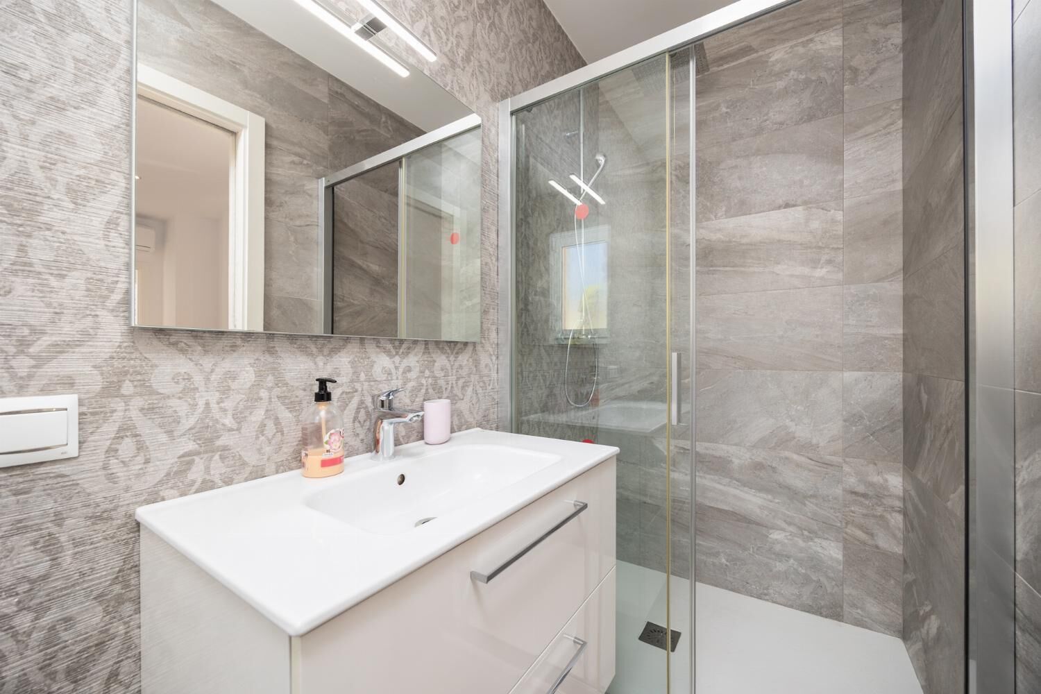 A modern bathroom with a glass shower enclosure, a white vanity, and a large mirror.