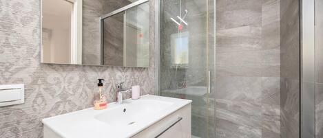 A modern bathroom with a glass shower enclosure, a white vanity, and a large mirror.