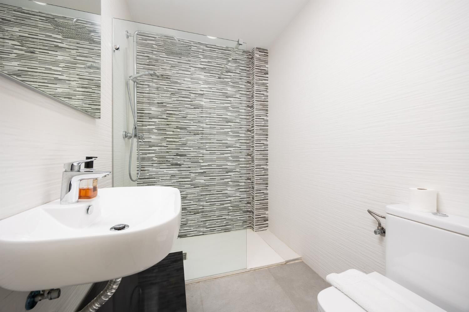 A modern bathroom with a glass shower enclosure, a white sink, and a toilet.