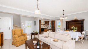 A living room with a sofa, armchair, and coffee table, a dining area with a table and chairs, and a kitchen in the background.