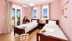 A hotel room with two beds, a wooden nightstand, a vanity with a mirror, and a view of the sea.