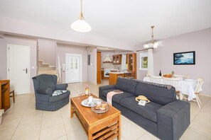 A living room with a sofa, armchair, and coffee table, a dining area with a table and chairs, and a kitchen in the background.