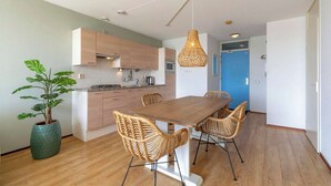 A modern kitchen with wooden cabinets, a dining table with wicker chairs, and a hanging light fixture. - Apartment in Groote Keeten Near the Beach (Callantsoog)