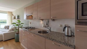 A modern kitchen with granite countertops, stainless steel appliances, and wooden cabinets. - Apartment in Groote Keeten Near the Beach (Callantsoog)