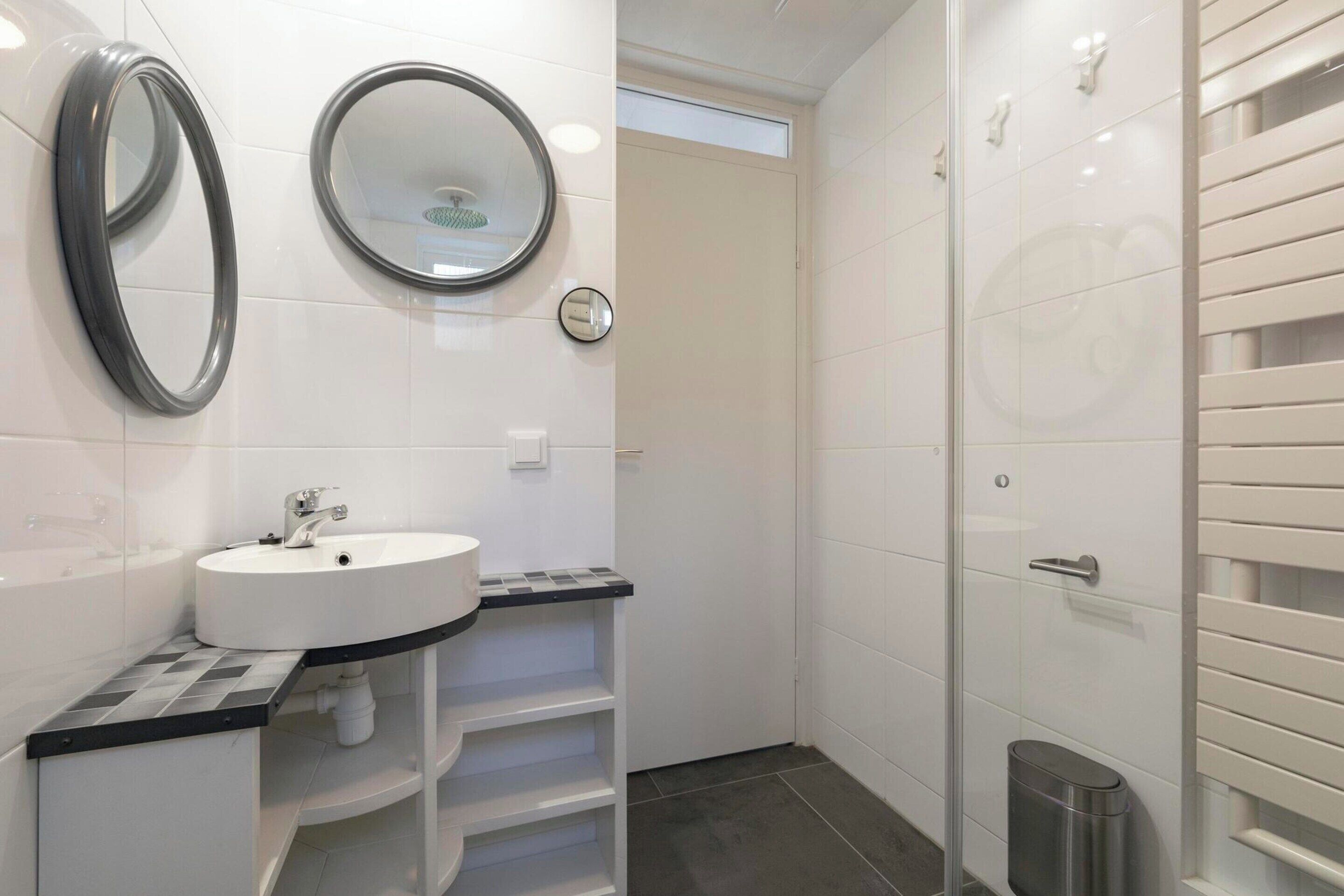 A modern bathroom with a white sink, two mirrors, a shower with a glass door, and a toilet.