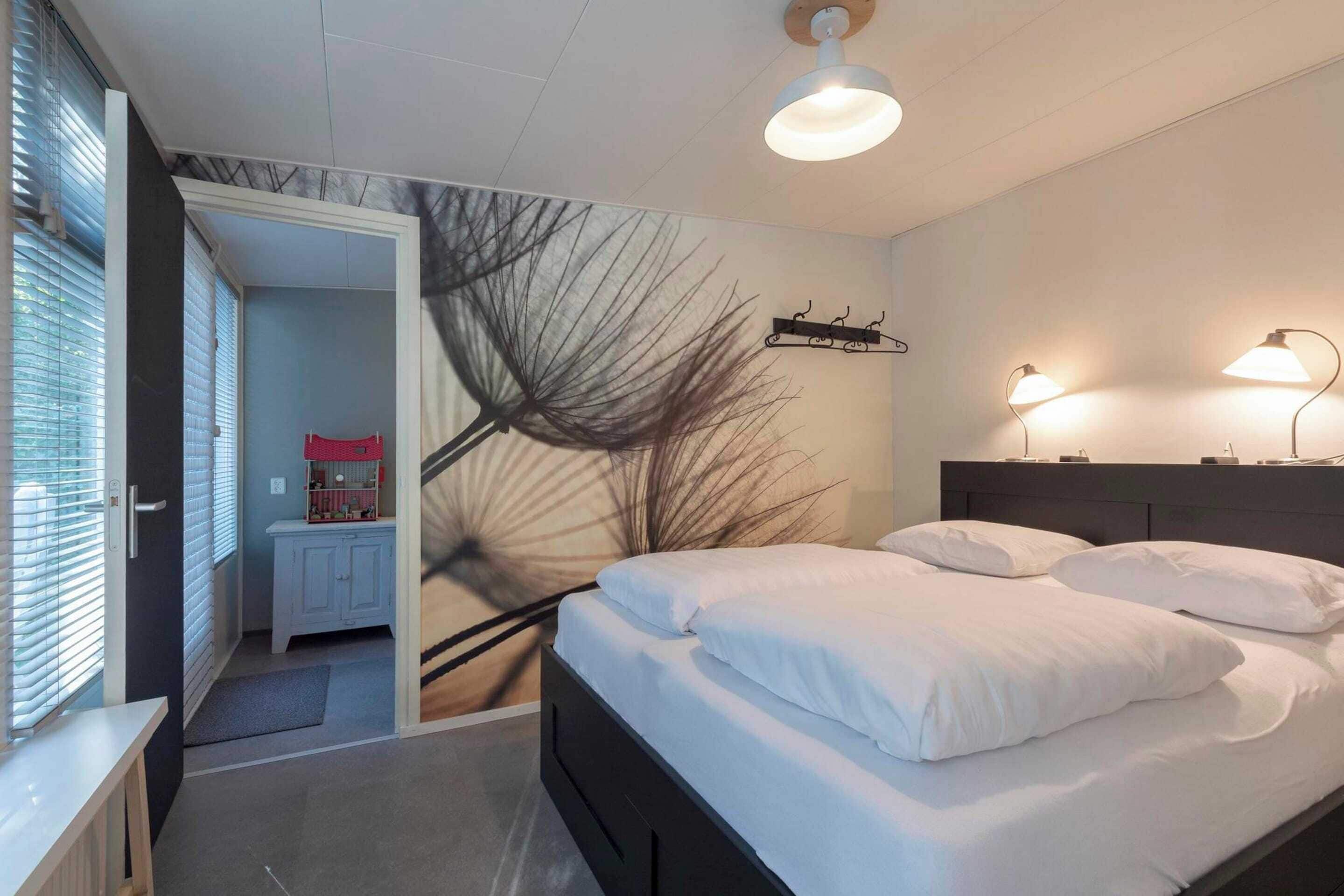 A bedroom with a bed, bedside lamps, a wall art piece, and a door leading to a bathroom.