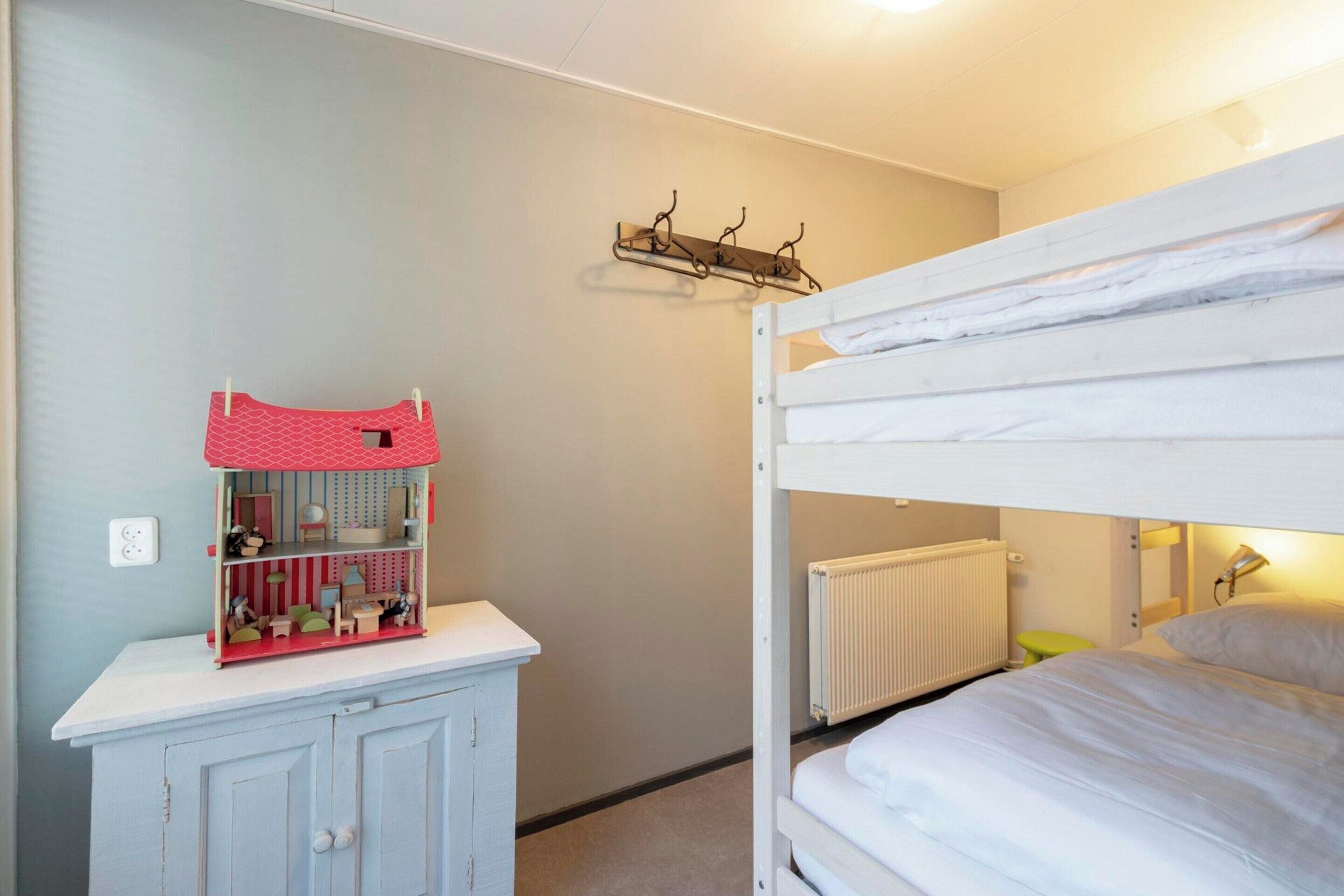 Ein Schlafzimmer mit Etagenbetten, einem Heizkörper, einem kleinen Tisch mit einer Puppenhaus und einem an der Wand befestigten Regal.