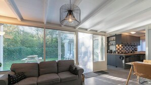 A modern living room with a sofa, coffee table, and a dining area with a chair. A kitchen is visible in the background. - Duinland 110 Bungalow in Sint Maartenszee (Sint Maartensvlotbrug)