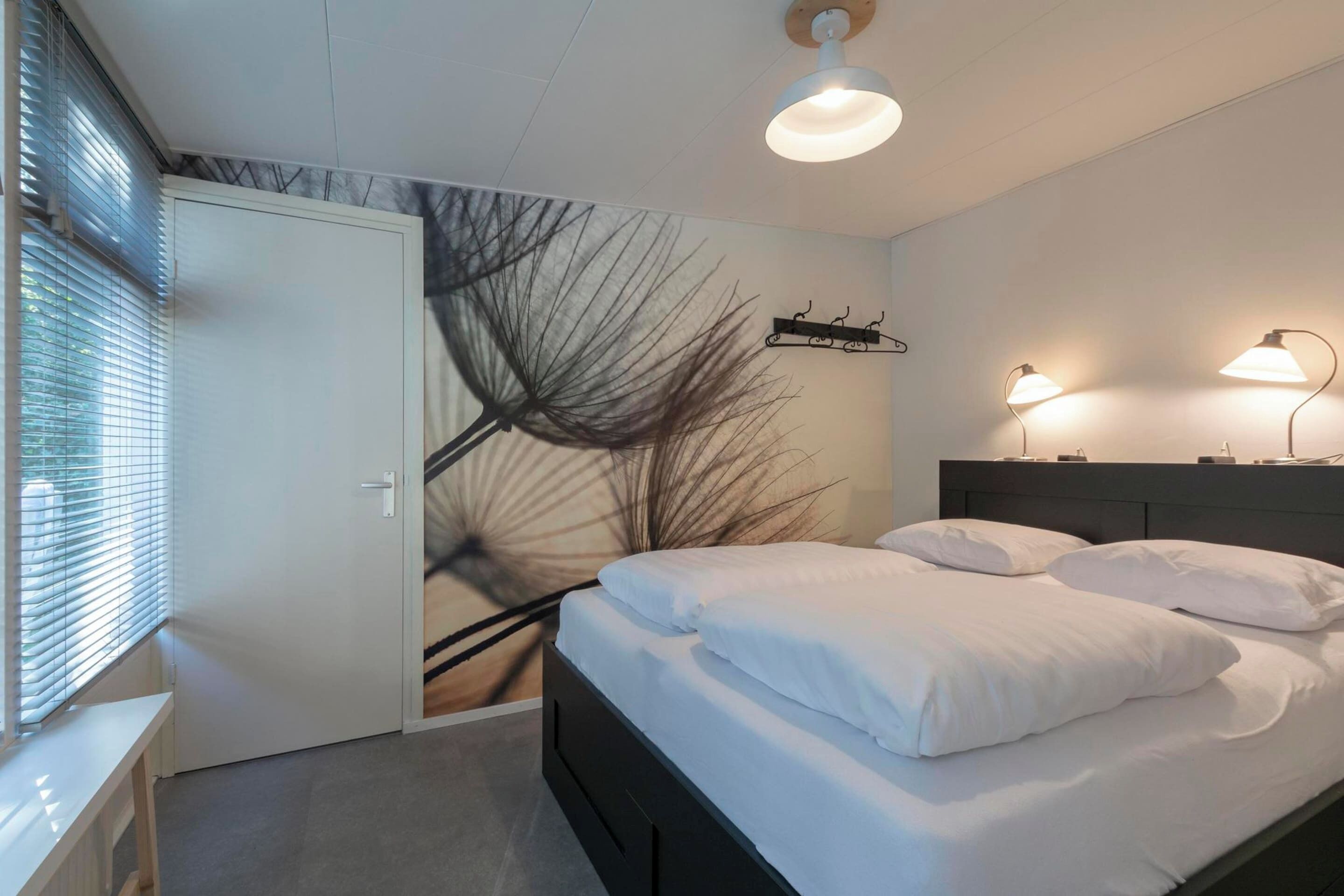 A bedroom with a bed, bedside lamps, a wall art piece, and a window with blinds.