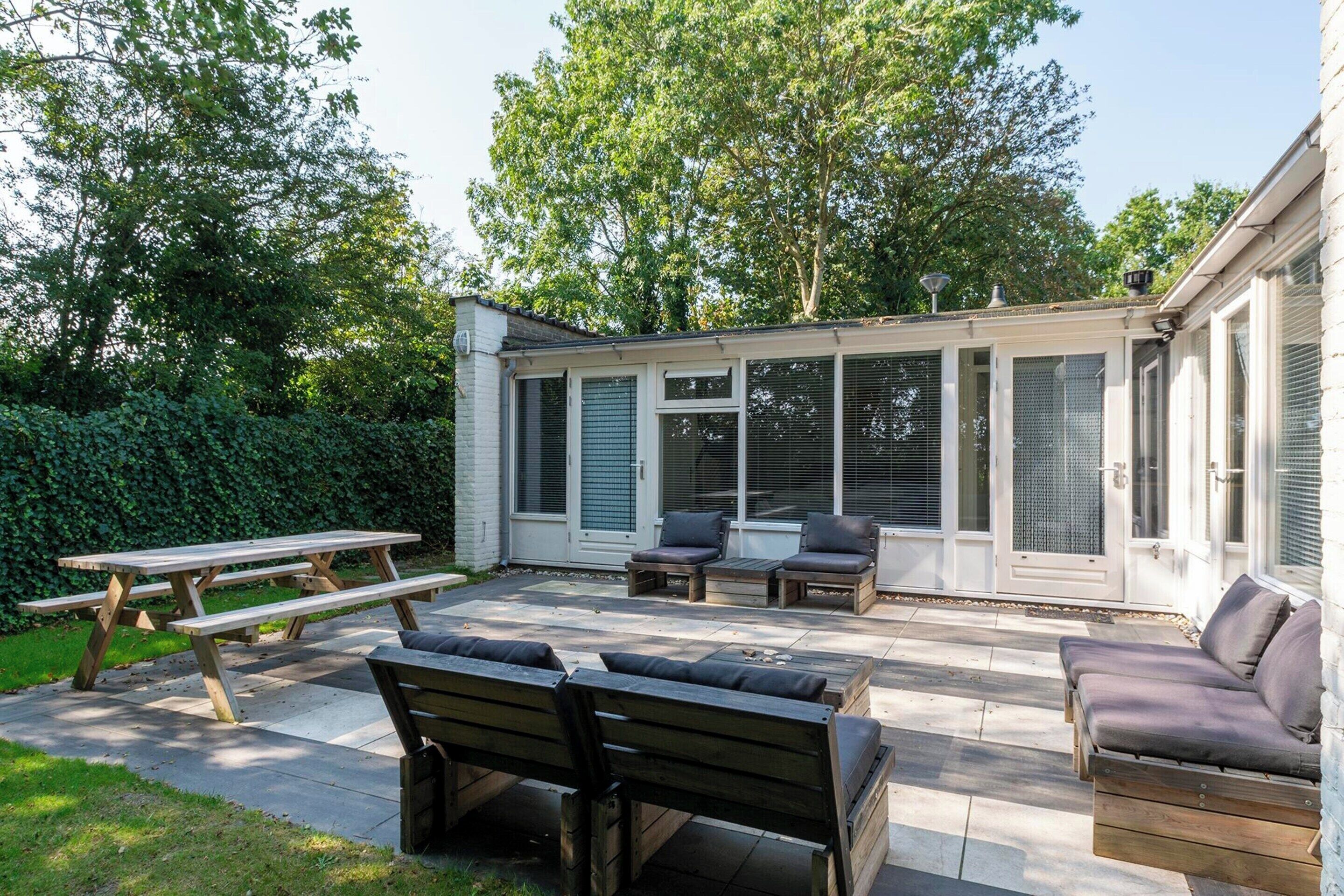 Un patio con muebles de madera, una mesa de picnic y un área cubierta con puertas corredizas de vidrio.