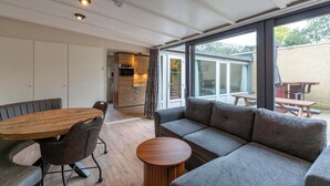 A modern living room with a wooden dining table, grey sofa, and a small wooden side table. - Bungalow Near Sint Maartenszee Beach (Sint Maartensvlotbrug)