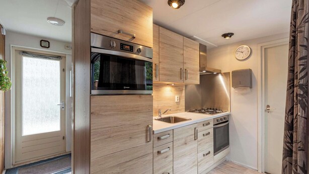 A modern kitchen with wooden cabinets, stainless steel appliances, and a clock on the wall. - Bungalow Near Sint Maartenszee Beach (Sint Maartensvlotbrug)