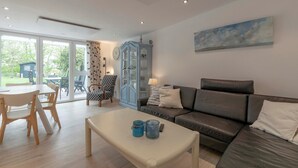 A modern living room with a sofa, a coffee table, and a dining area with chairs and a table. - Duinland 146 for 4 Guests With Garden (Sint Maartensvlotbrug)