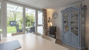 A dining area with a table, chairs, a cabinet, and a clock on the wall. - Duinland 146 for 4 Guests With Garden (Sint Maartensvlotbrug)