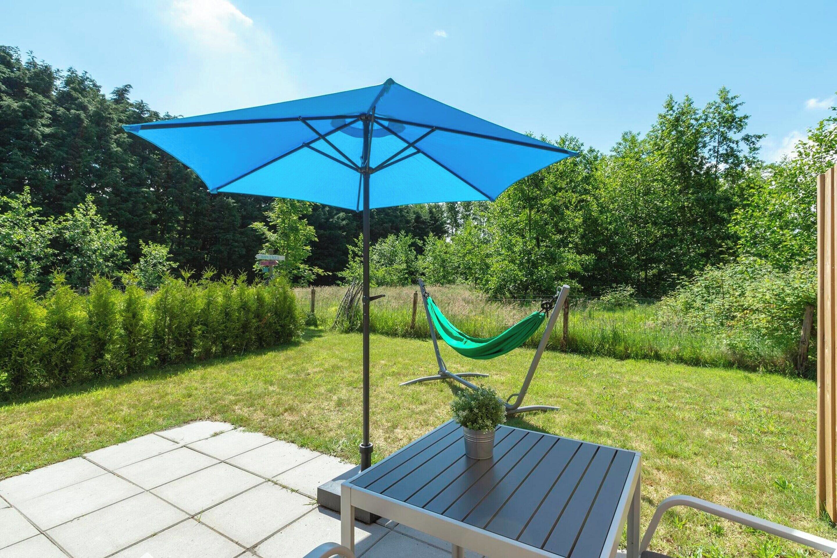 A patio with a table, a blue umbrella, and a hammock.
