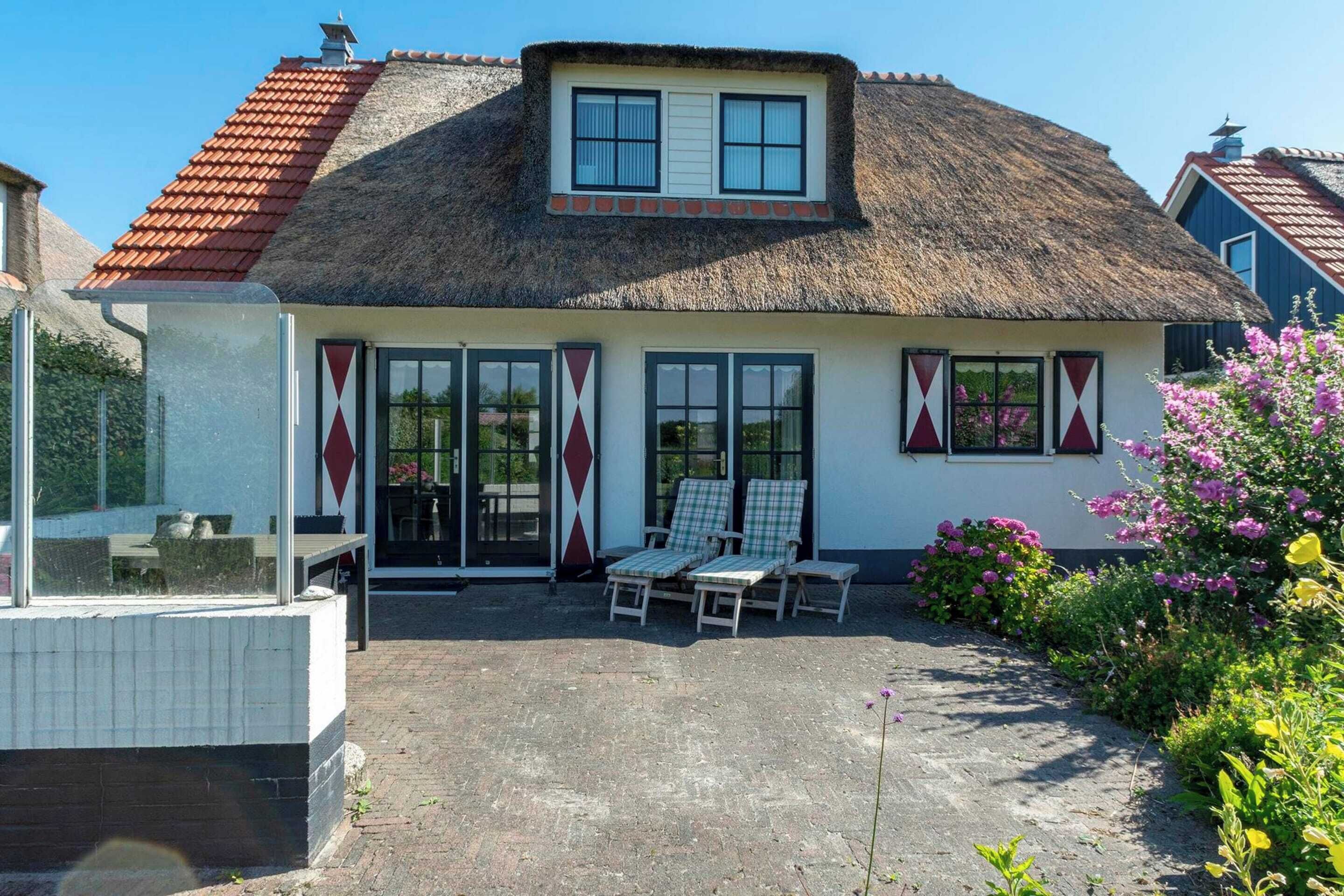 A house with a thatched roof, a small balcony, and a garden with flowers.