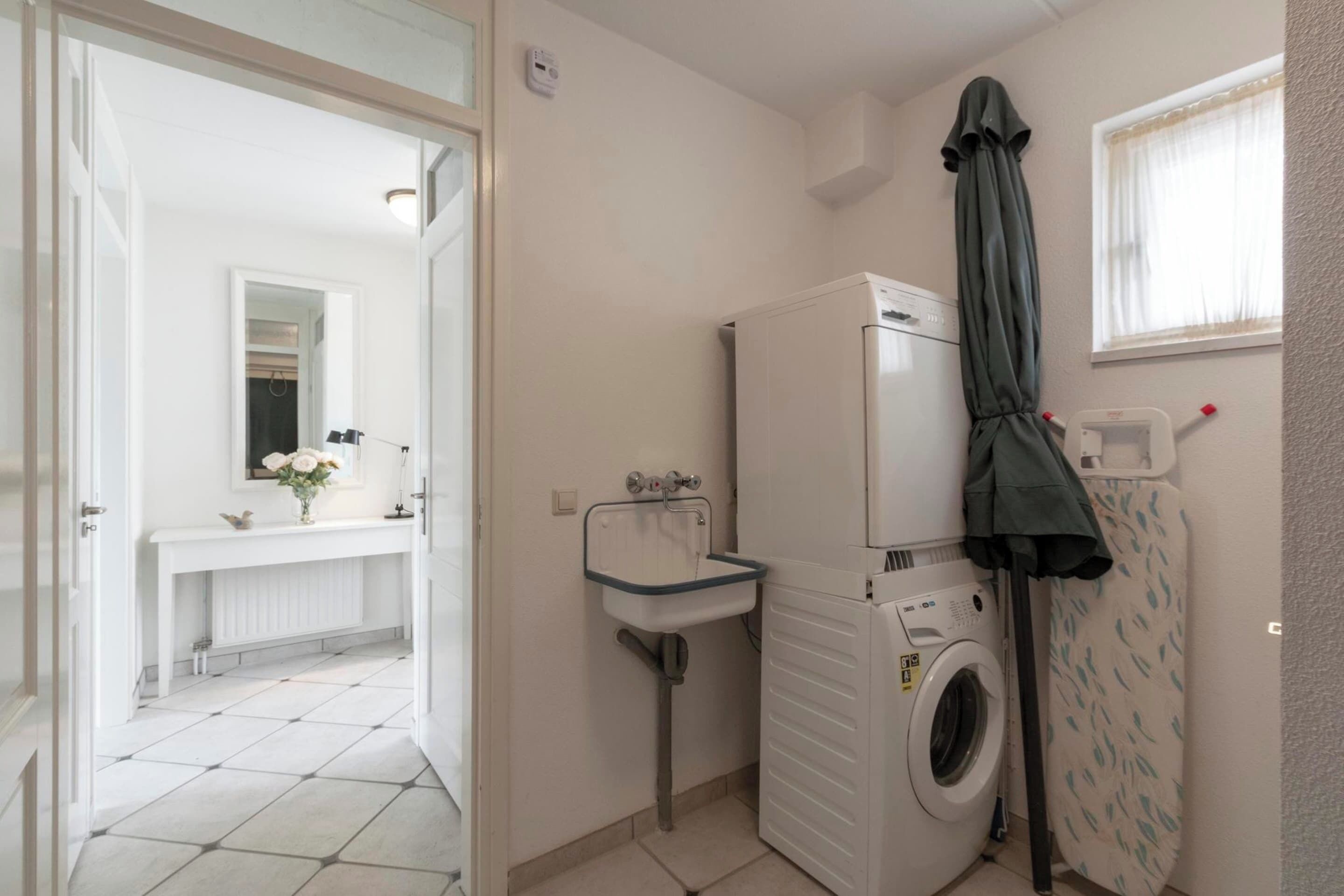 Een kleine wasruimte met een wasmachine, een wasbak en een droogrek.