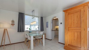 A modern kitchen with white cabinets, a dining area with a glass table, and a large wooden cabinet. - Holiday Home St. Maartenszee Near Beach (Sint Maartensvlotbrug)