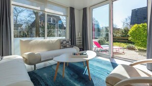 A modern living room with a sofa, a coffee table, and large windows offering a view of the outdoors. - Holiday Home St. Maartenszee Near Beach (Sint Maartensvlotbrug)