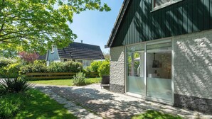 A modern house with a stone exterior, large glass doors, and a paved driveway leading to a wooden deck. - Holiday Home St. Maartenszee Near Beach (Sint Maartensvlotbrug)