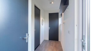Un pasillo estrecho con paredes de colores oscuros y claros, una puerta con manija y una lámpara en el techo.