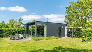 Una casa moderna con un porche acristalado, una chimenea y un jardín con mesa y sillas.