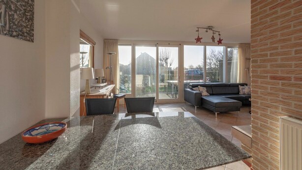 A modern living room with a sofa, a dining area with a table and chairs, and a large window with a view of the outside. - Callantsogervaart 3-8 Home Near Beach (Julianadorp)