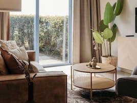 A modern living room with a sofa, a round coffee table, and a large window overlooking a garden.