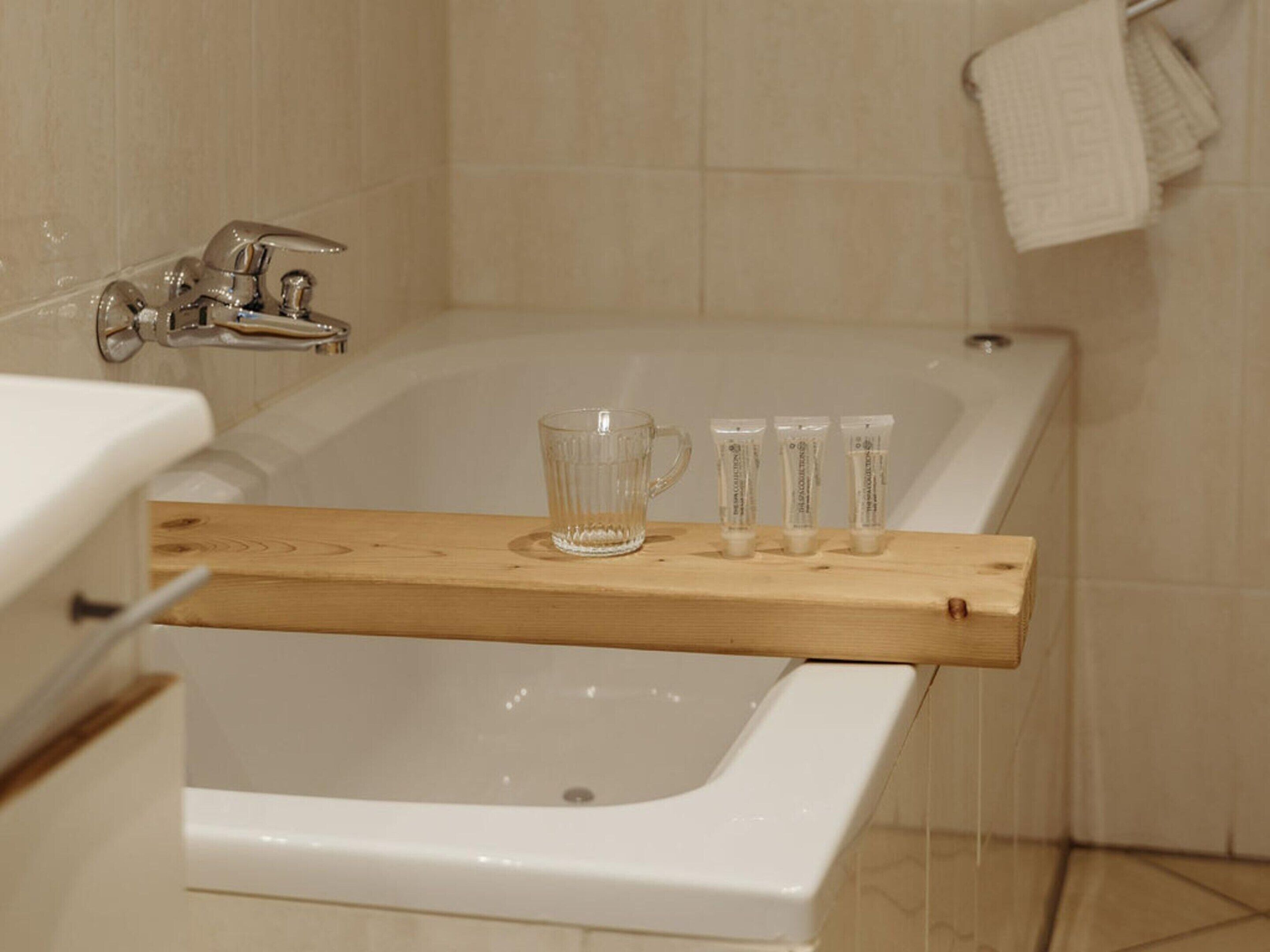 Un baño con una bañera, un estante de madera con tres vasos de vidrio y un lavabo blanco.
