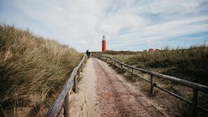 A brick pathway leading to a red lighthouse with a person walking away. - Apartment in Netherlands Near the Coast (De Cocksdorp)