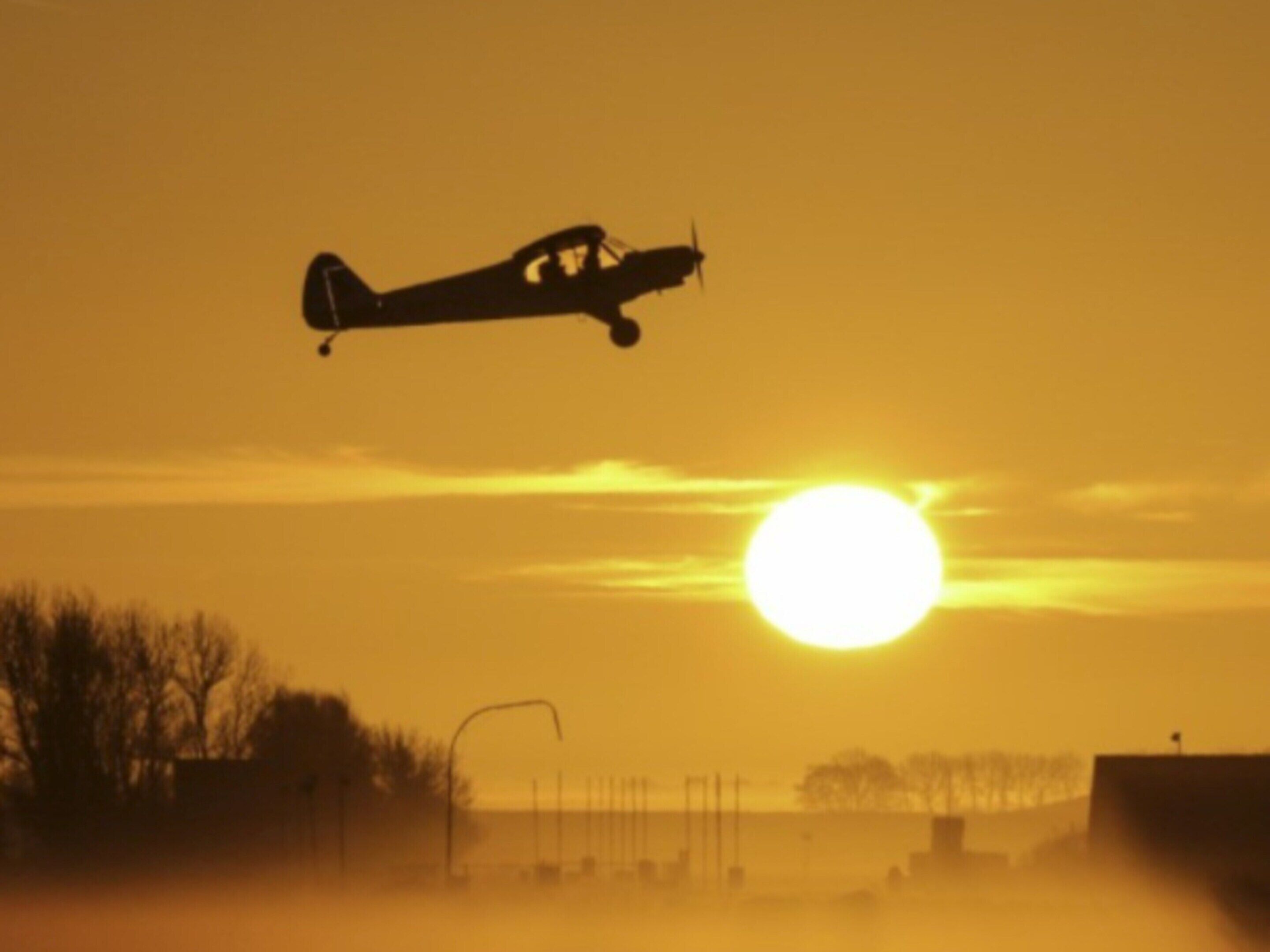 A small airplane flying near the sun with a clear sky.